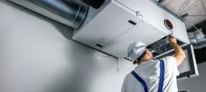 An HVAC engineer is installing a heat recovery ventilation system on an air conditioning unit.